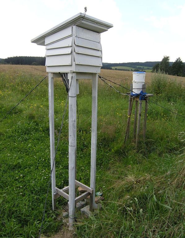 Meteorologick� budka (teplom�r, vlhkom�r), na st�e�e sol�rn� �idlo, pod budkou minim�ln� teplom�r, �idla na m��en� teploty p�dy. V pozad� sr�kom�r.